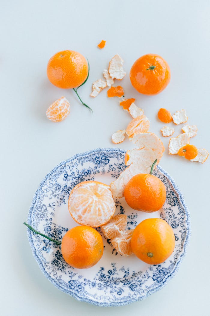 Top view of vibrant mandarins on a floral ceramic plate with a light background.